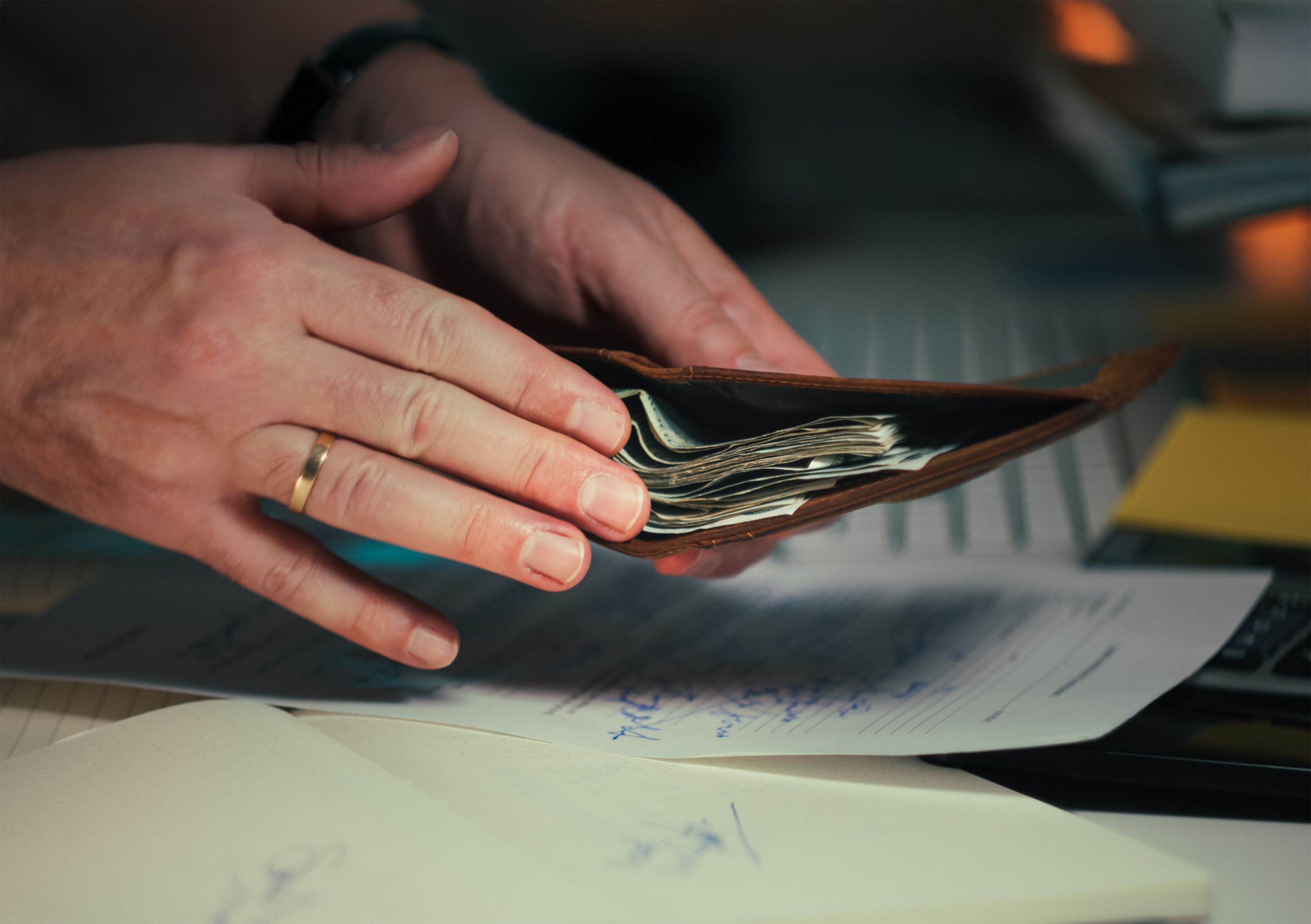 Hands holding a leather wallet of currency over signed documents