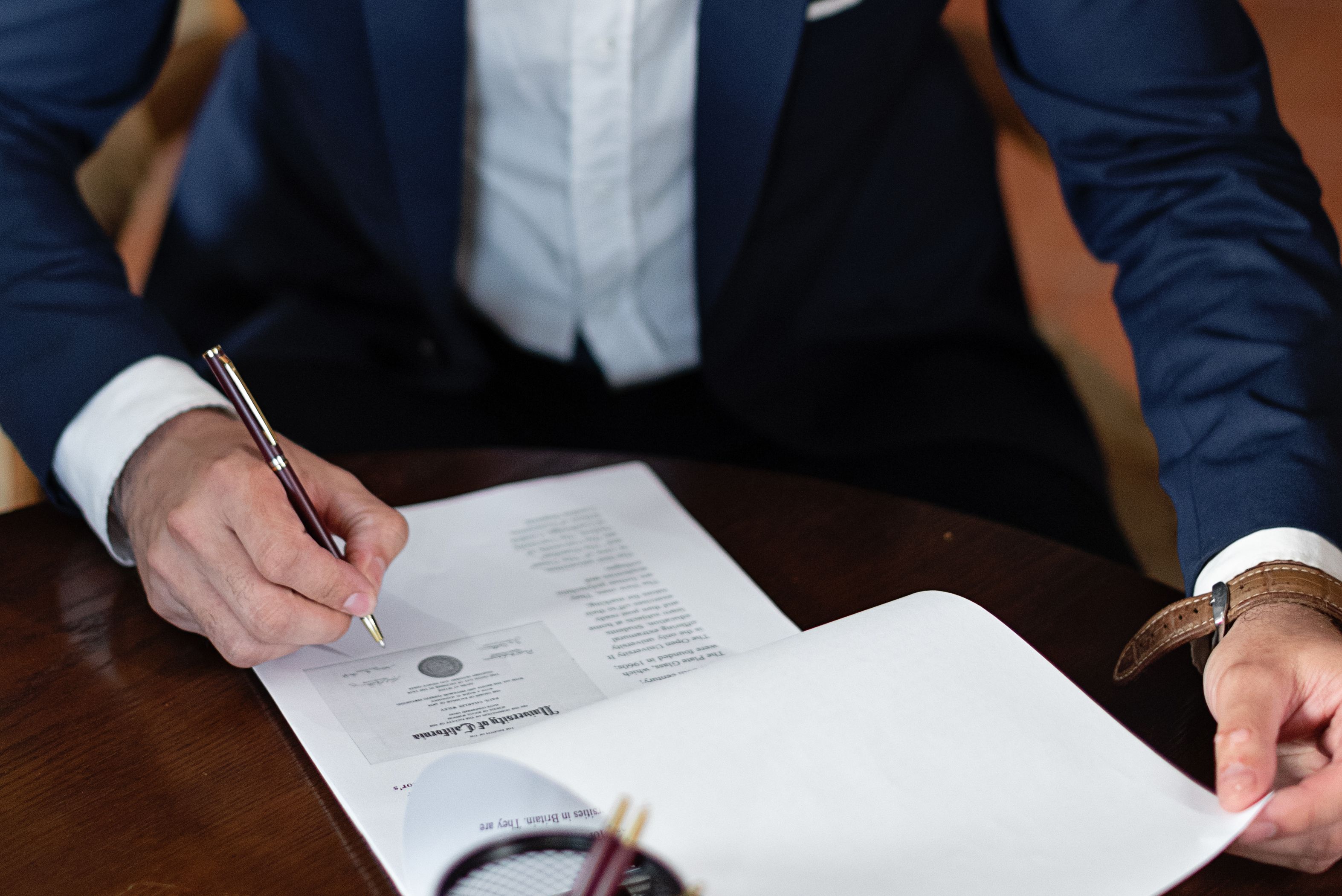 Hands signing a formal instrument at a desk